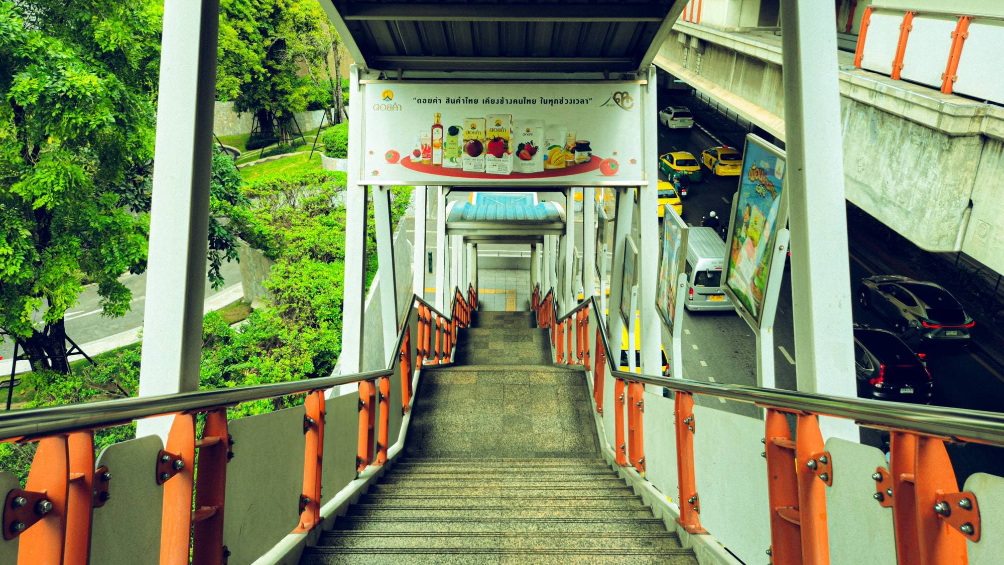 A covered footbridge stair going down to a street, orange railings, taxis below
