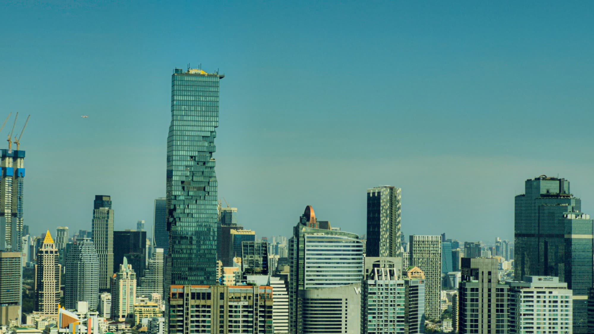 A tall glass tower among other high-rises under a blue sky