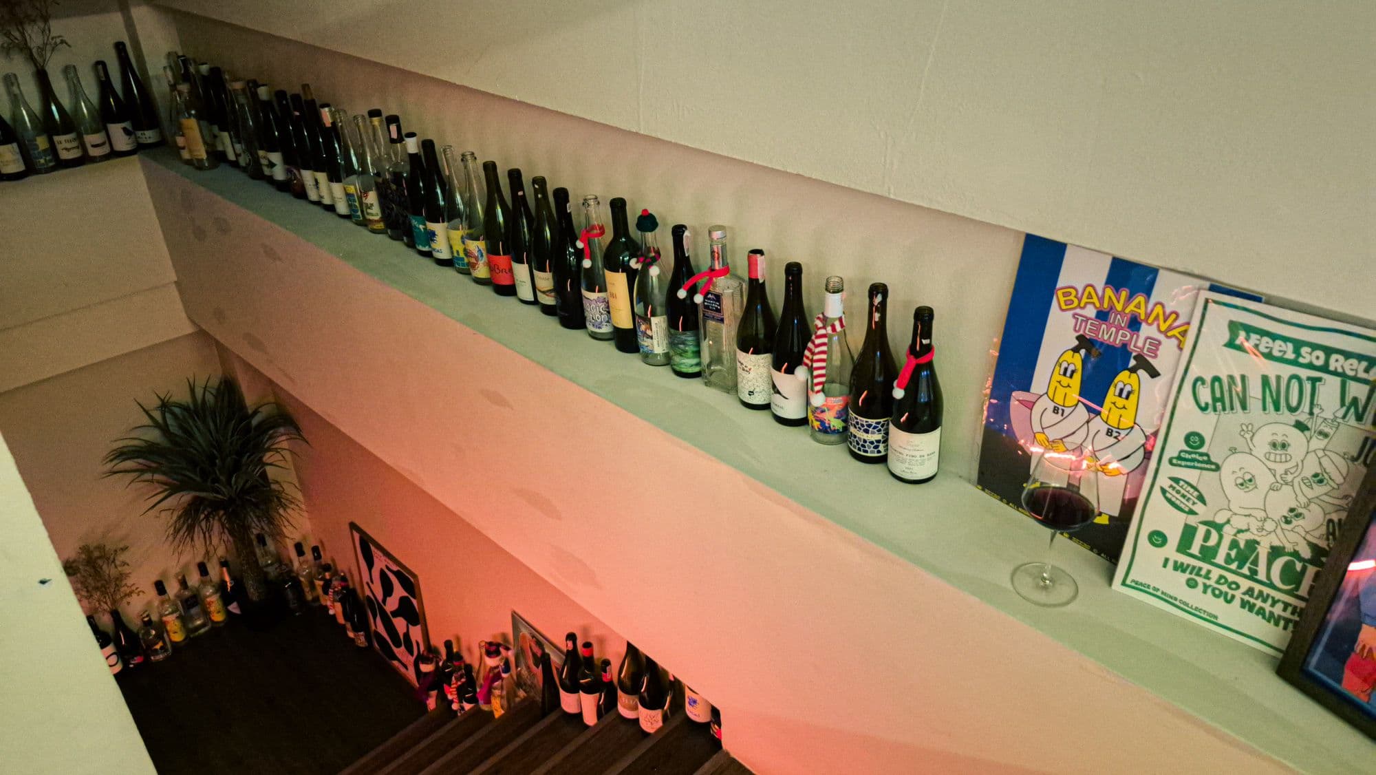 Wine bottles lined along a ledge seen from above, posters at the end of it