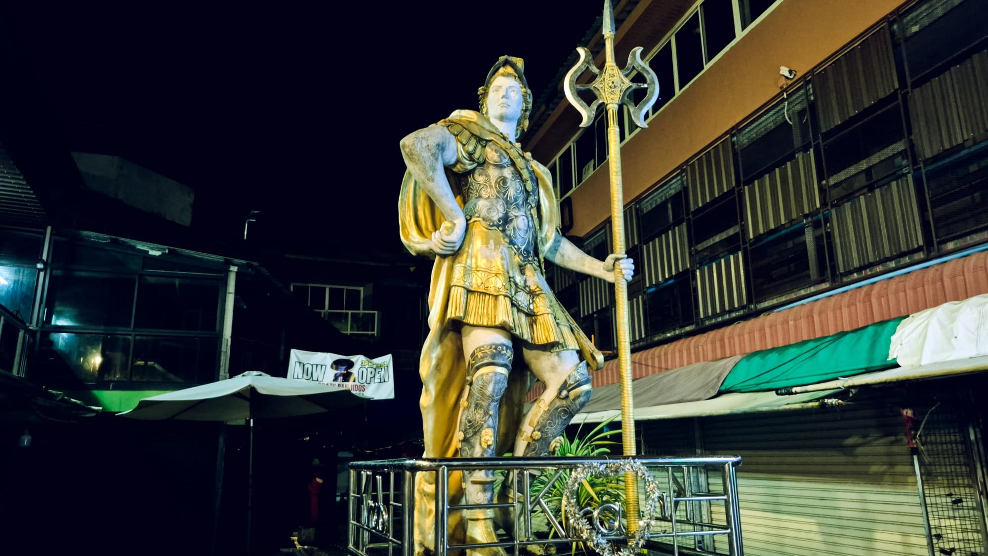 A gilded statue of a soldier in armour with a halberd, in a dark street at night
