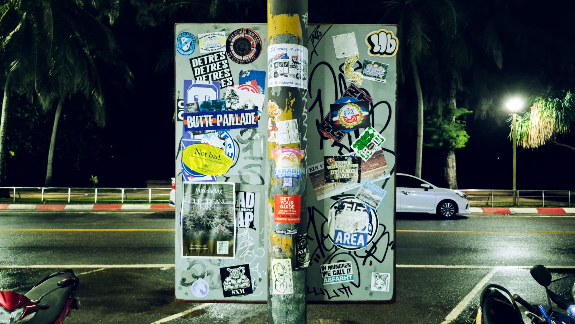 A pole and a board covered in stickers at night, palm trees behind