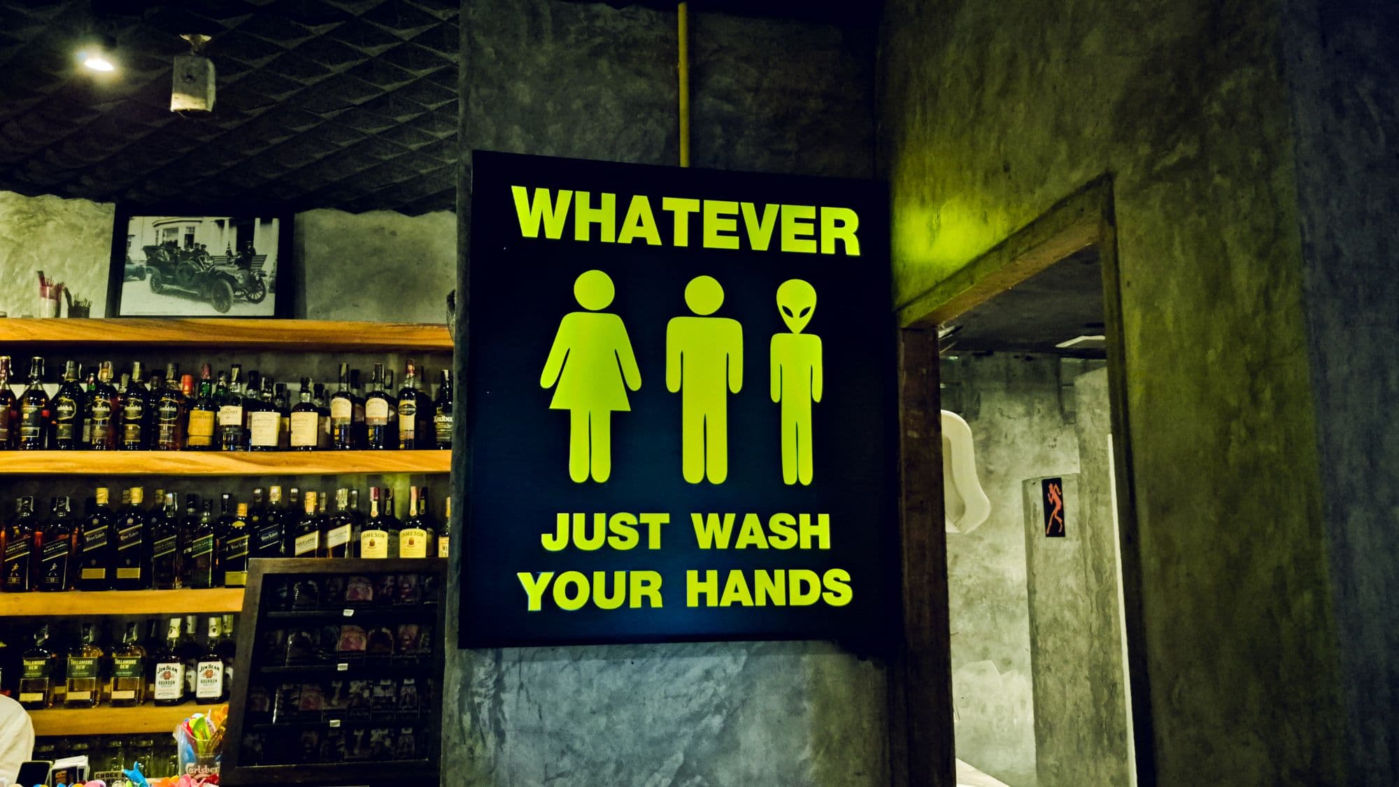 A lit sign reading "Whatever, just wash your hands", with a woman, a man and an alien