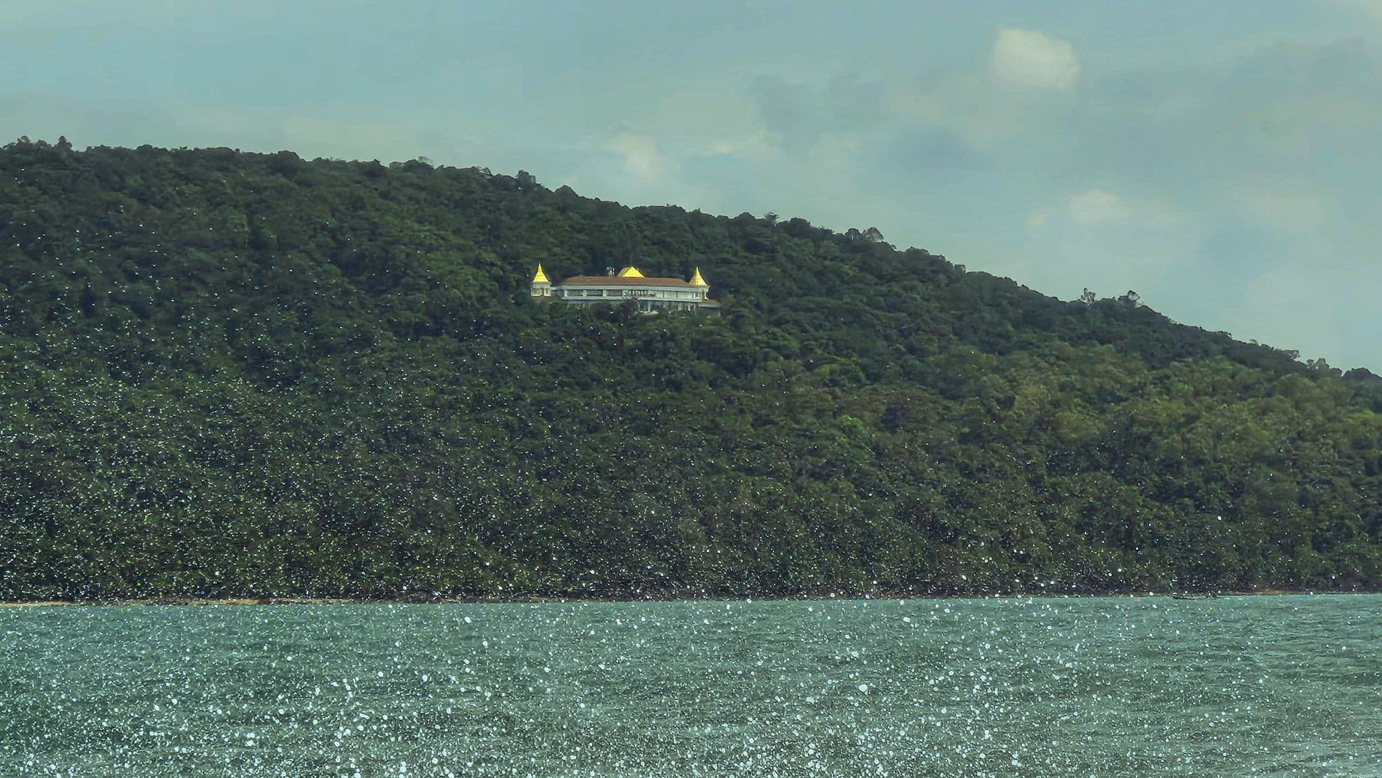 A forested hill above the sea with a small white building with gold spires