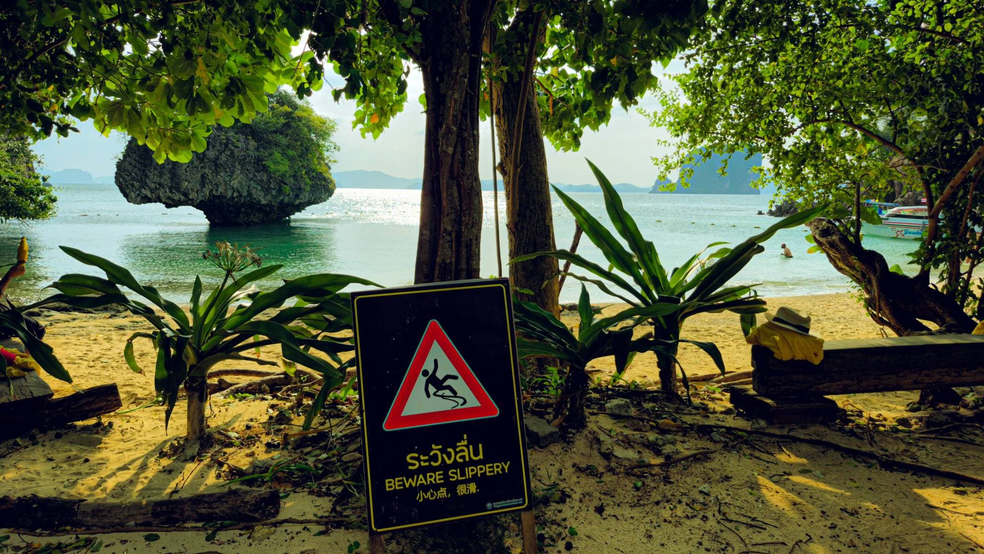 A "Beware slippery" sign on a beach, a rock islet in the water behind