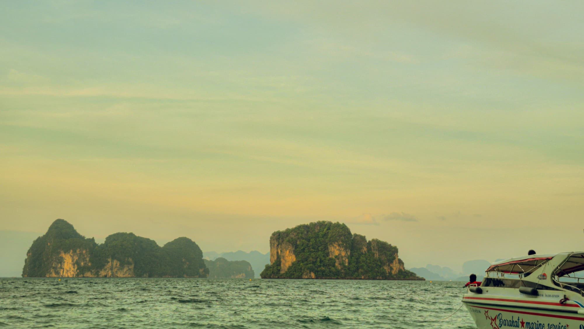 Green limestone islands at dusk, the bow of a speedboat at the edge of the frame